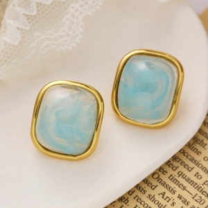 Détail de clous d'oreilles carrés dorés avec texture marbrée bleu clair sur fond vintage