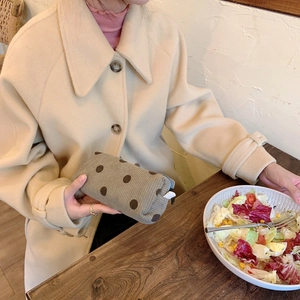 Detailed close-up of a corduroy polka dot pouch held by a model in a cozy cafe setting
