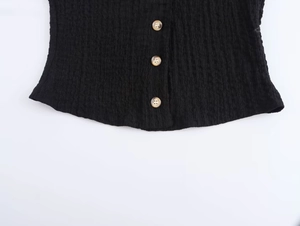 Detail of black textured bubble crepe fabric vest with faux wood buttons and ruffled hem