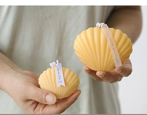 Close-up of hands holding two yellow shell-shaped scented candles in large and small sizes