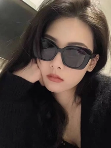 Close-up of model wearing black oversized cat-eye sunglasses with dark grey lenses