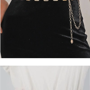 Detailed view of a gold metal chain belt accessory on black velvet dress fabric