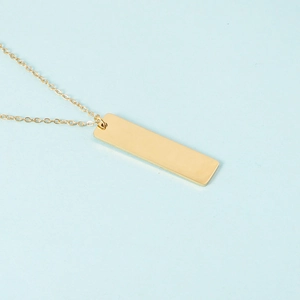 Detailed close-up of polished gold rectangular bar pendant necklace on blue surface