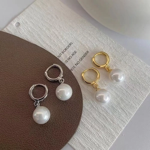 Detail of gold and silver hoop earrings with white pearls on a textured background