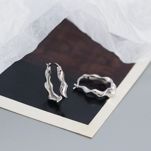 Macro detail of silver twisted hoop earrings with a wavy texture and minimalist design