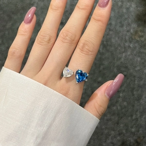 Detail of adjustable silver ring with blue and clear heart-shaped zircon stones on finger