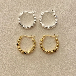 Detail of silver and gold S925 sterling silver geometric bead hoop earrings on beige surface
