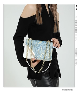 Detail view of stylish white crossbody bag with blue gold textured flap and metal chain strap