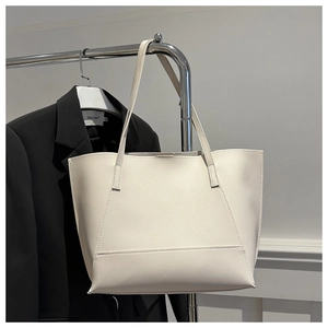 Detail of minimalist beige leather tote bag hanging against a classic black blazer
