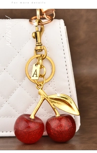 Macro shot of red glitter cherry bag charm with golden leaf and letter A tag on a bag