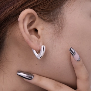 Close-up of heart-shaped hollow silver earring with mirror finish on model ear