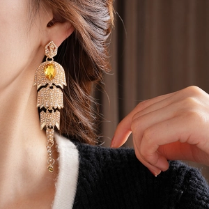 Detail of vintage gold pearl earrings with yellow rhinestone fishbone tassels on a model