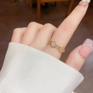 Close-up of a gold four-leaf clover ring with white shell and zircon on a finger