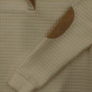 Dettaglio del tessuto a maglia trapuntato beige con toppa marrone sul gomito della felpa