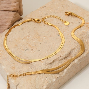 Polished double-layered golden flat snake chain necklace and bracelet set on stone