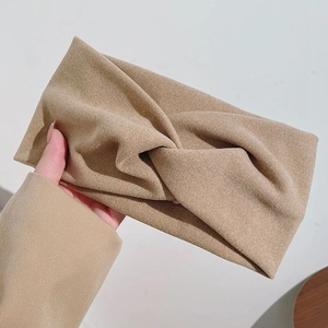 Gros plan d'un bandeau en daim kaki avec un design élégant à nœud croisé tenu à la main