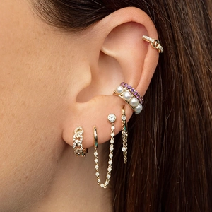 Detailed view of layered gold earrings featuring pearls, diamonds and chain tassels