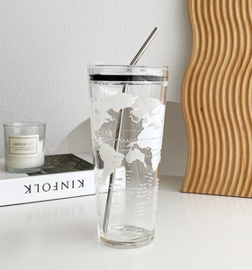 Detail of a large glass tumbler with white world map print and metal straw on a desk