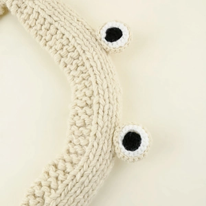 Detailed macro view of the cream-white chunky knit headband with cute frog eye decorations