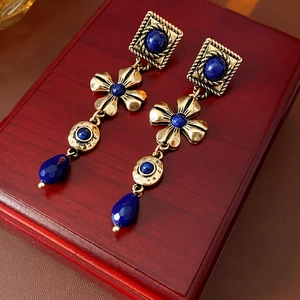 Detailed shot of vintage gold flower earrings with blue crystal drops on wooden box