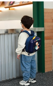 Detail of child wearing blue hard shell dinosaur backpack with musical cartoon print