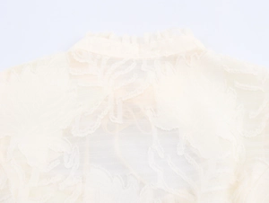 Detailed close-up of ruffle collar and jacquard textured fabric on a cream blouse