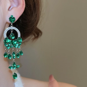 Detail of elegant emerald drop earrings with silver tassels worn by a model