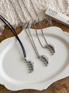 Detail of vintage silver comb pendant necklaces on an elegant white embossed ceramic plate