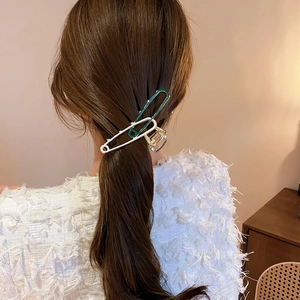 Detail showing geometric pin-shaped hair clips in white, green, and gold on dark hair