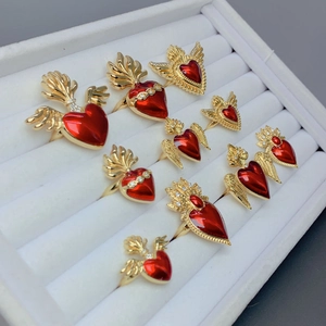 Macro detail of nine gold rings with red enamel hearts and wings set in a white jewelry box