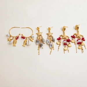 Dettaglio di orecchini boho dorati con perle di corallo rosso e conchiglie naturali