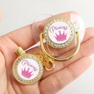 Detailed view of a golden rhinestone pacifier set featuring a pink princess crown design