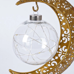 Détail d'une lampe en métal doré en forme de lune avec motifs ajourés et boule LED en verre