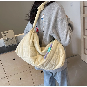 Detail of cream quilted tote bag featuring a knotted wide shoulder strap on a model