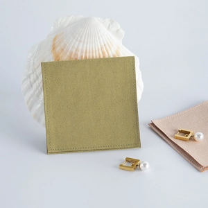 Close-up of golden pearl earrings on olive green velvet pouch with a white shell