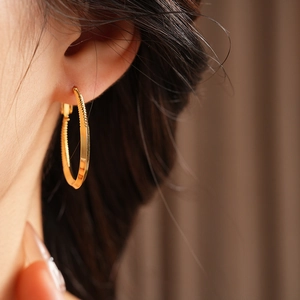 Close-up of a twisted gold hoop earring with textured detail worn by a model