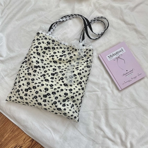 Detail of floral canvas tote bag with white lace trim and black ribbon bow accents