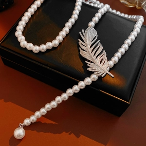 Macro detail of elegant pearl necklace with diamond-encrusted feather pendant on leather