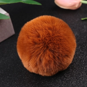 Detailed view of an 8cm brown faux rabbit fur pom pom on a dark textured background