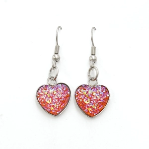 Close-up of heart-shaped stainless steel earrings with sparkling orange glitter inlay