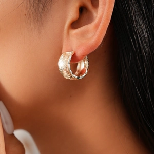 Close-up of gold hoop earrings with feather texture on a model's ear lobe