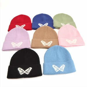 Flat lay of knit beanies in 8 colors featuring white butterfly jacquard patterns