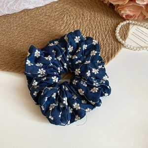 Detail of navy blue pleated scrunchie with white floral embroidery on woven mat