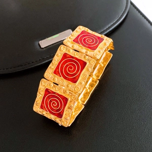 Detail of vintage gold bracelet with red enamel squares and spiral patterns on leather