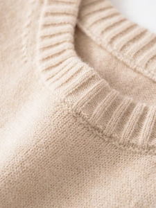 Close-up of the finely ribbed crew neck collar on a beige knit sweater with soft texture