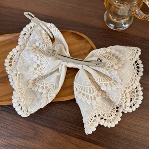 Detailed view of white lace bow hair clip with metal spring on a wooden tray