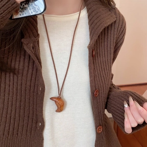 Detailed view of creative croissant food pendant on a dark brown cord worn on a model