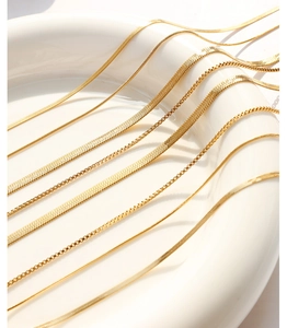 Detailed macro view of layered gold snake chains and box chains on white ceramic