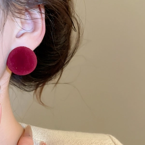 Detailed close-up of a red flocked velvet stud earring on a model for autumn style