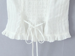 Close-up of white smocked top featuring intricate ruffles and drawstring lace-up details